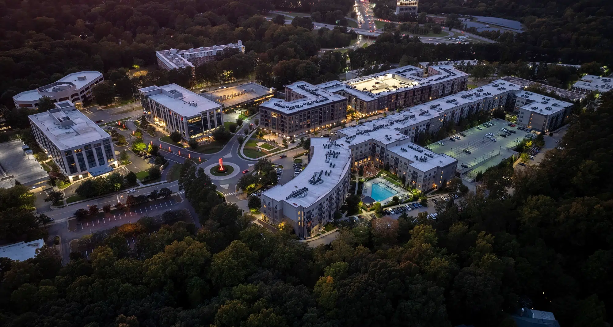 Aerial nighttime view of a modern urban complex with illuminated buildings, streets, and green spaces