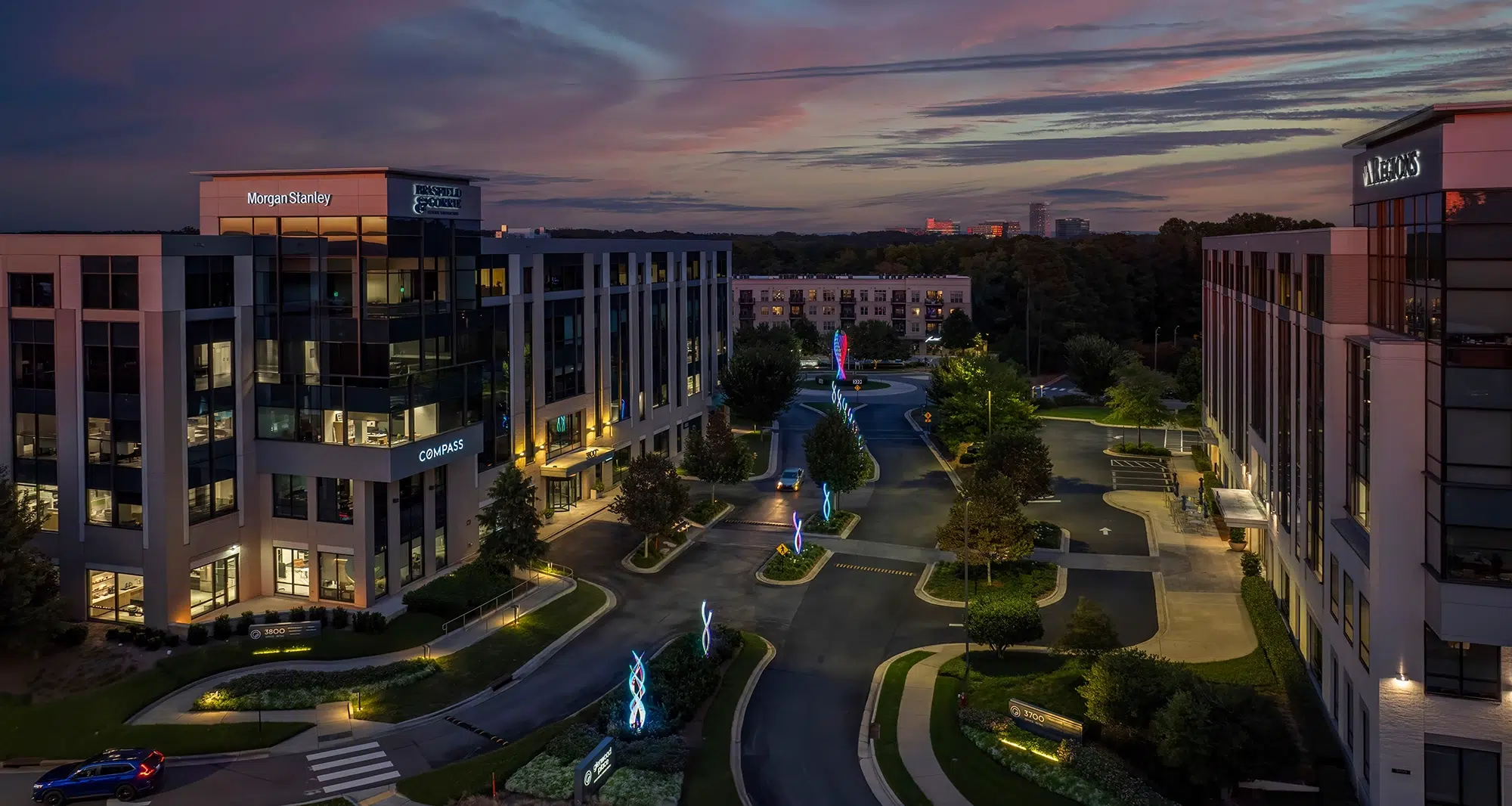 Twilight cityscape featuring modern offices, street lighting, and artistic neon sculptures along the road