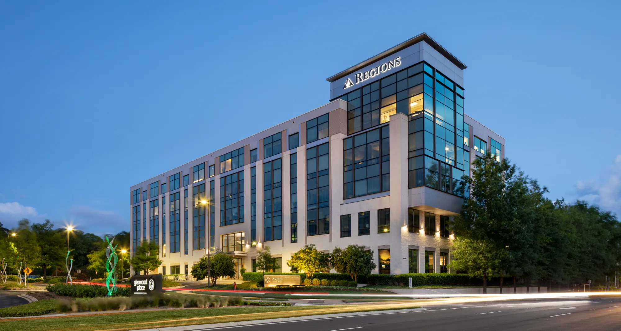 A sleek, glass-fronted office building at dusk, with an illuminated Regions Bank logo