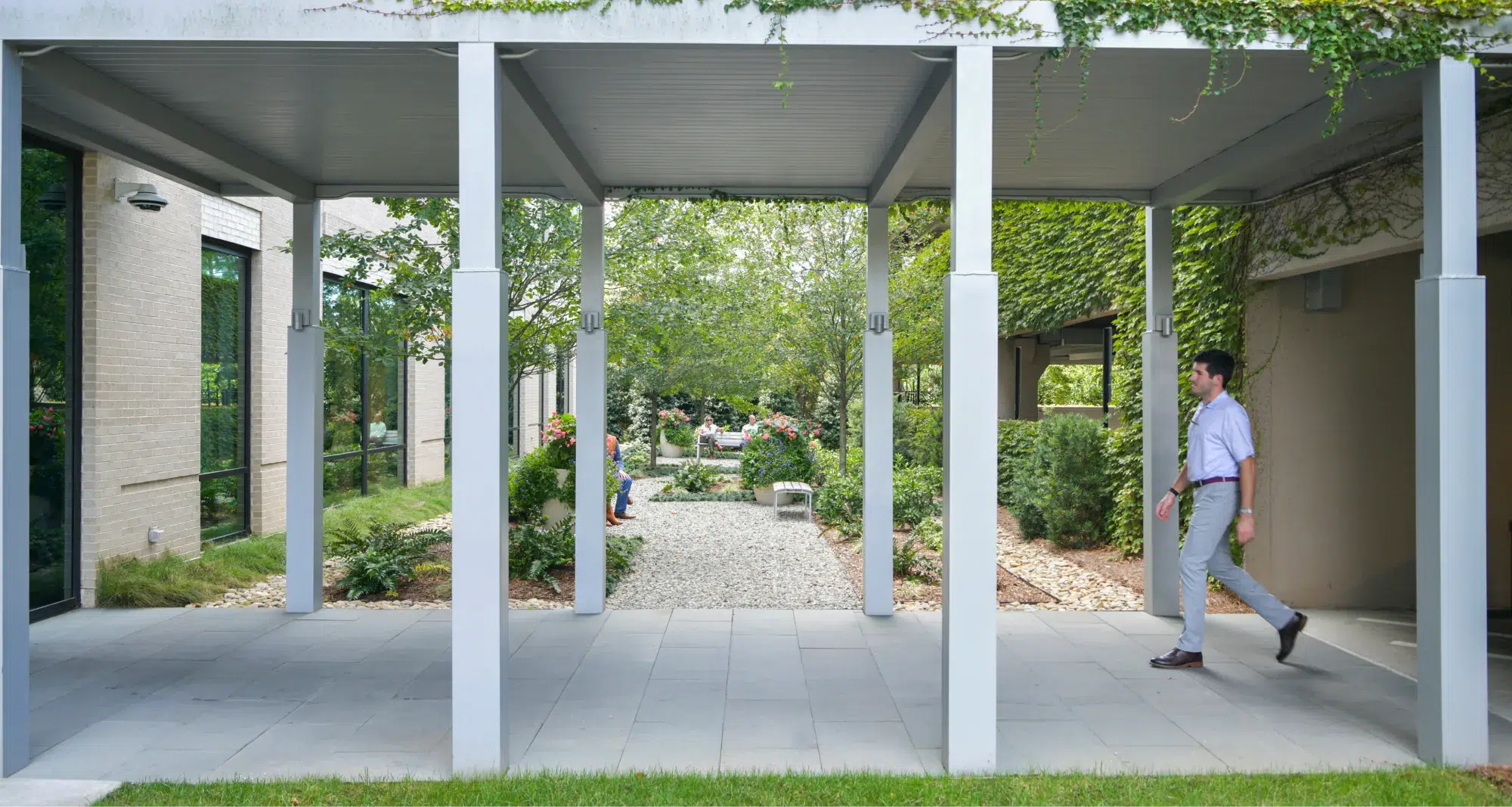 Man walking along a shaded pedestrian corridor with ivy-covered walls