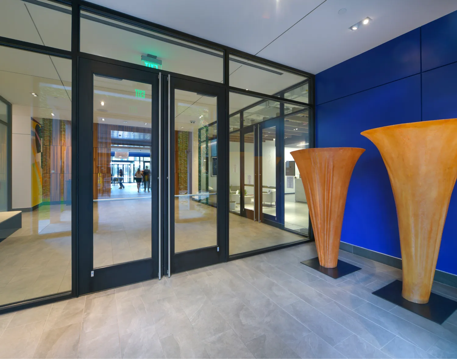 Two large orange sculptures with flared tops placed against a dark blue wall in a modern lobby