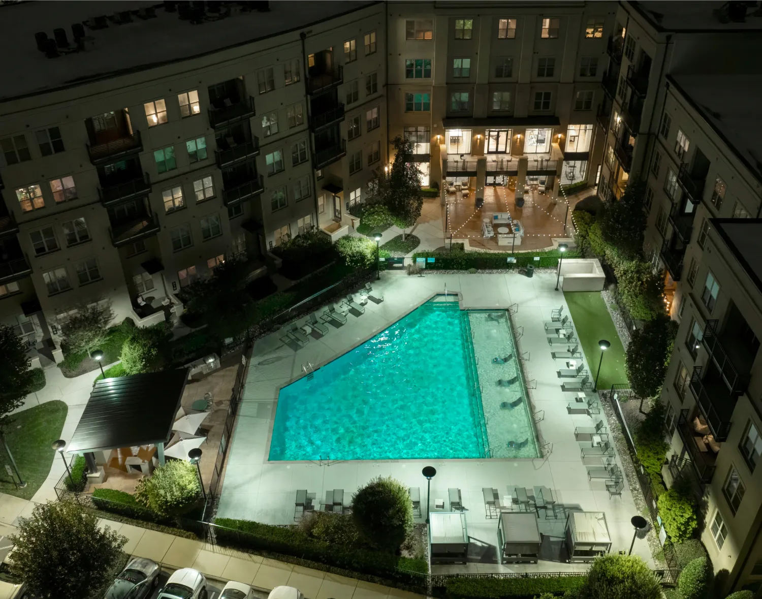 Aerial night view of a luxury apartment complex with a glowing outdoor pool and stylish courtyard