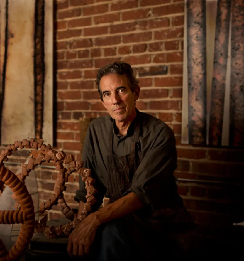 Sculptor Thomas Sayre in his workshop, posing with his intricate, industrial-inspired sculpture pieces.