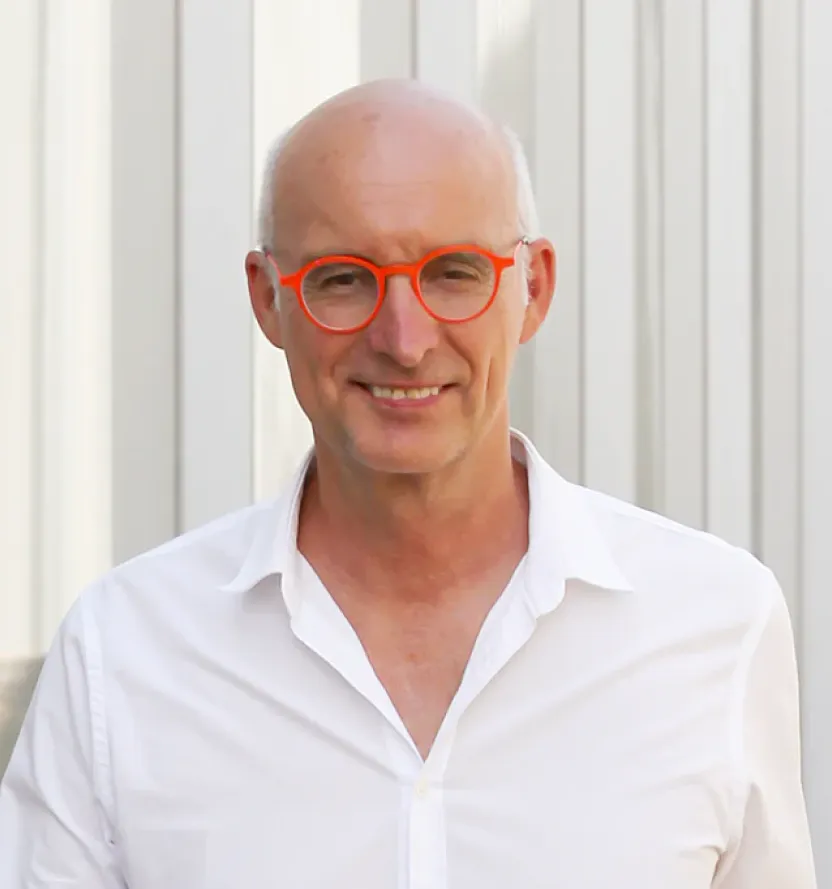 Portrait of Randy Schull in a crisp white shirt and bold orange glasses, smiling outdoors