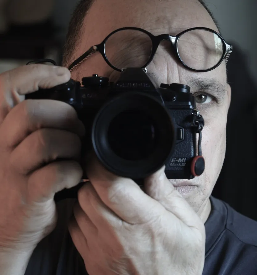 Close-up portrait of photographer Dan Gottlieb aiming his camera, wearing glasses on his forehead