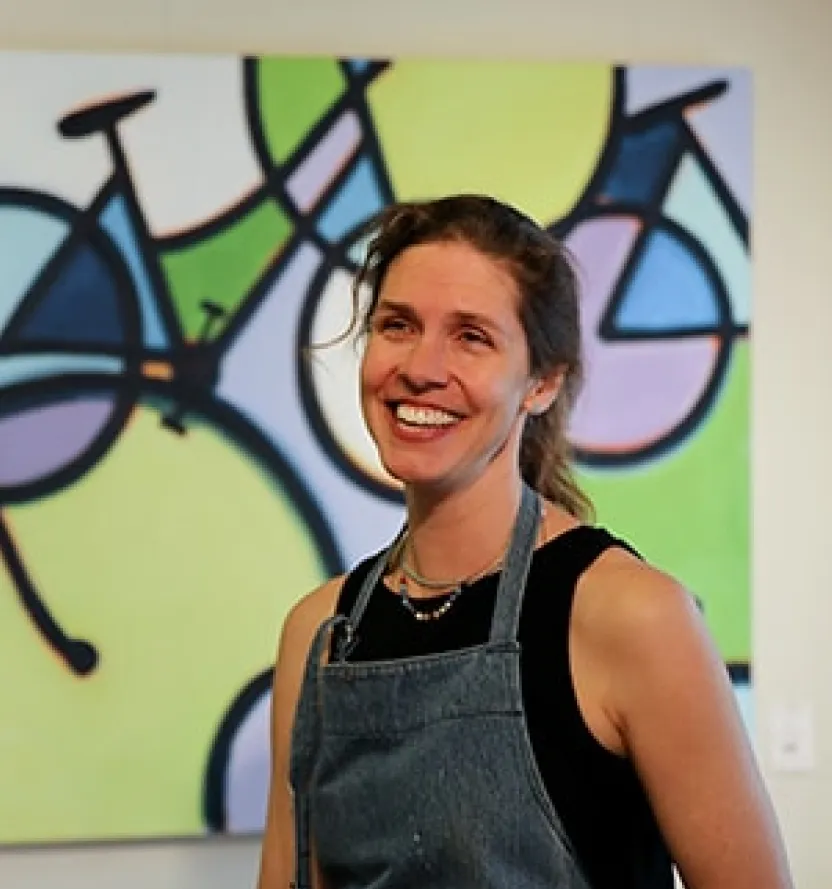 Playful portrait of artist Amber Cobeland with a bicycle-themed painting in the background