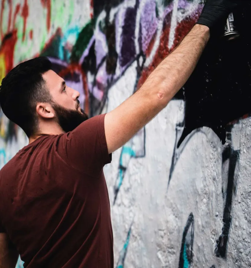 Artist Morgan Cook spray-painting a graffiti mural on an urban wall with bold colors.