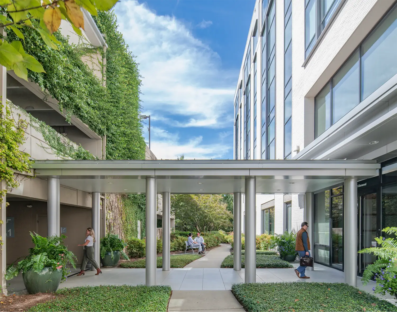 Covered walkway leading to a glass office building with lush greenery