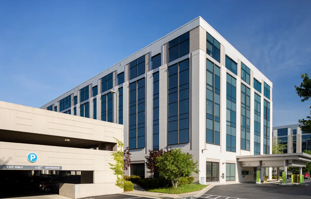 Modern glass office building with an attached parking garage under a clear sky